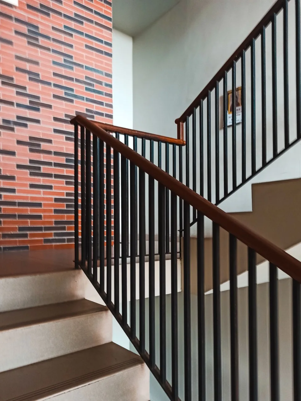 Escalera de un edificio de viviendas con barandilla de madera y pared de ladrillo visto